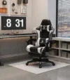 כיסא גיימינג Tesla דגם 7008 בגוון שחור-לבן בפינת עבודה עם שולחן מחשב, שעון דיגיטלי על הקיר וחלון עם וילון פסים